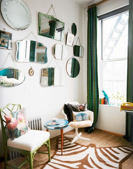 a quirky space with a mirror gallery wall with mismatching no frame mirrors, white chairs, layered rugs and green curtains
