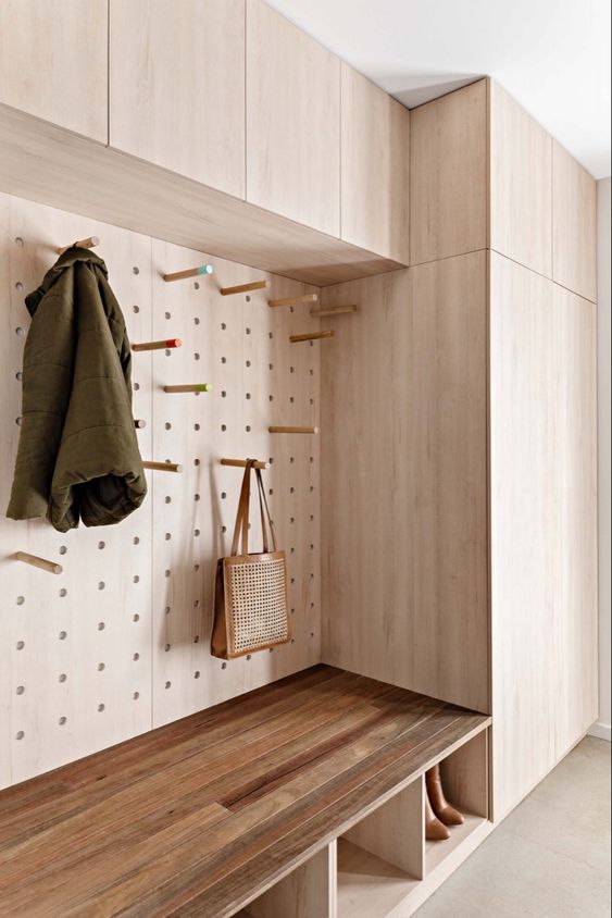 a refined and sleek modern entryway with stained cabinets and a pegboard with hooks that are used for storing some stuff