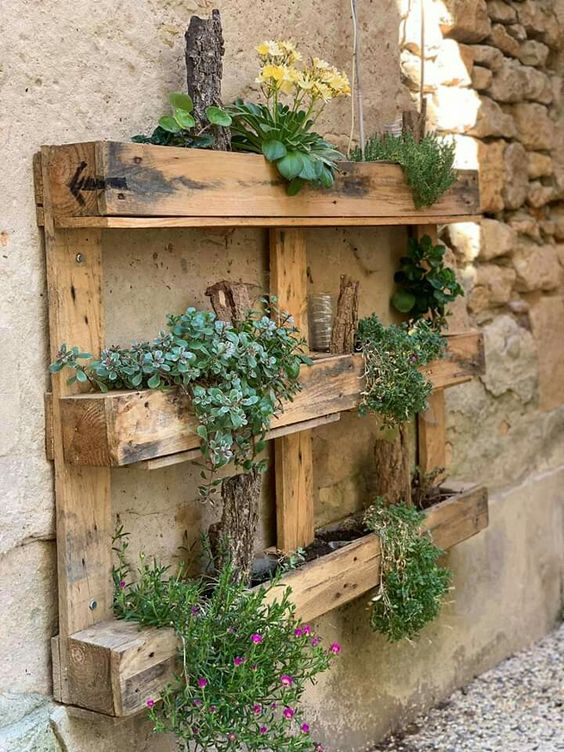 a rustic pallet garden with blooms and greenery attached to the wall is a cool decoration for a relaxed and rustic space