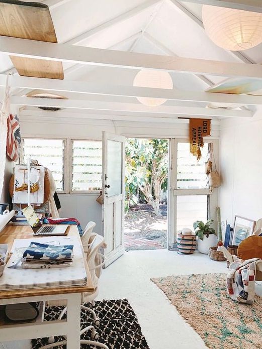 a shed home office with a desk, white chairs, boho rugs, shelves, decor and some stuff right on the floor