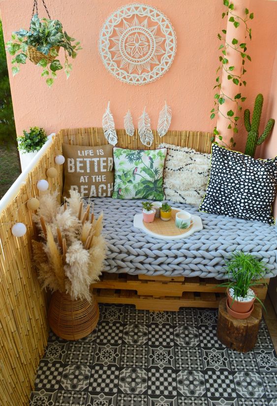 a small and cute boho balcony with a pallet loveseat, potted plants, some pillows and pampas grass in a basket
