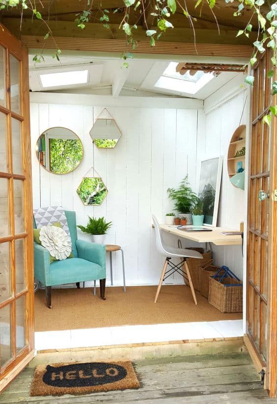 a small and cute shed home office with a gallery wall of mirrors, an aqua chair, a wall-mounted desk and a white chair