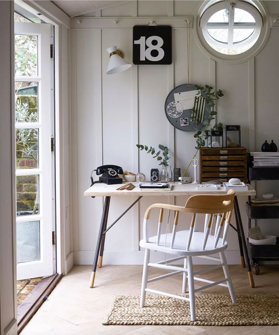 a small and pretty garden home office with a desk and a modern chair, black and white decor, a file cabinet and some greenery