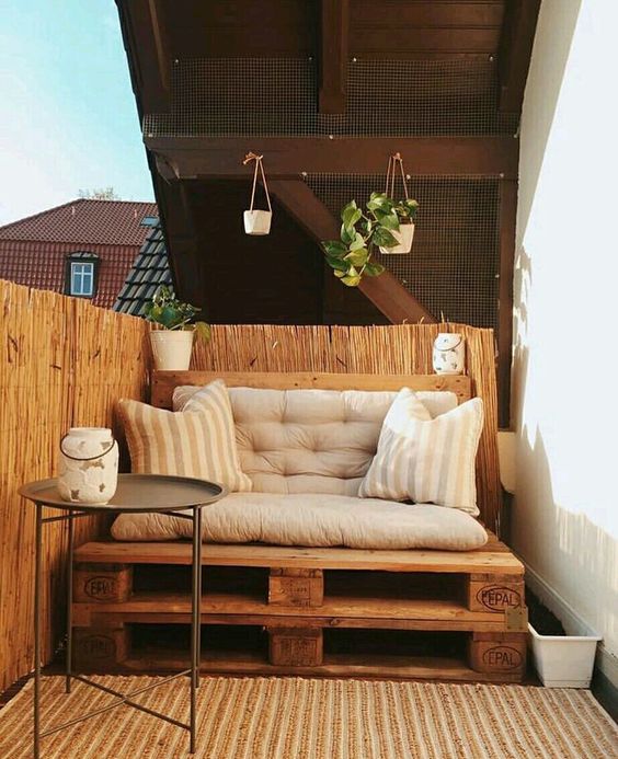 a small balcony with a pallet loveseat, a side table and some potted greenery is a cool and chic space