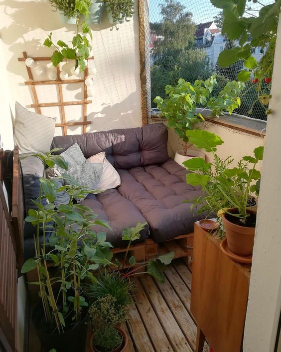 a small balcony with a pallet loveseat, potted greenery and lights is a lovely space to chill in