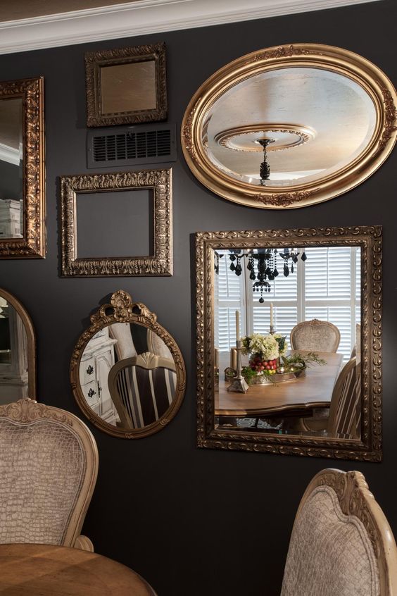 a sophisticated dining room with grey walls, a table and chic chairs, a gallery wall with mirrors and refined gold frames for an even more chic look