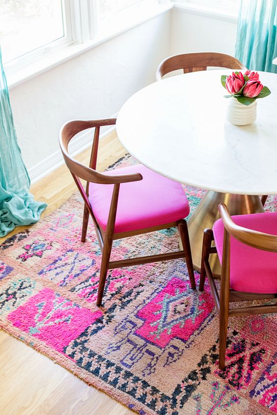 a stylish dining nook with a bold pink rug and matching chairs, a white table and turquoise curtains is amazing