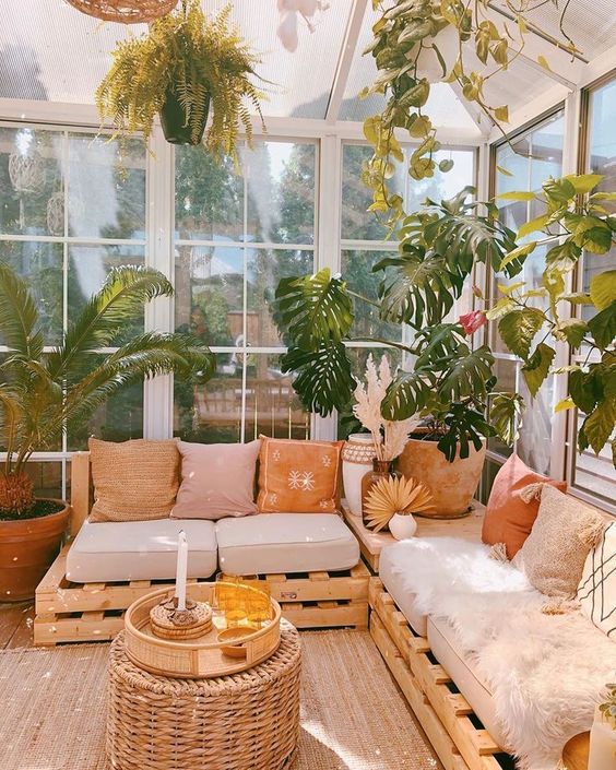 a sunroom with a pallet sofa with lots of pillows and cushions, potted plants and a wicker table