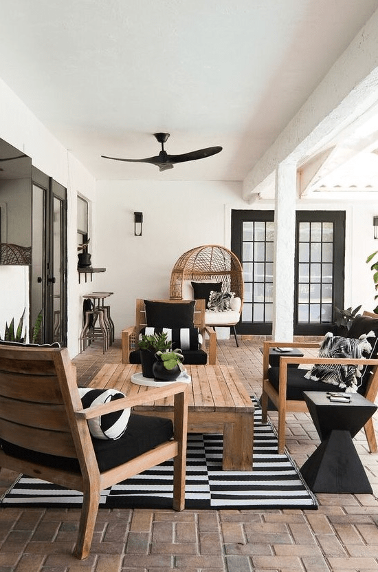 a super elegant modern farmhouse terrace with stained furniture, black and white textiles, an egg chair, a wooden coffee table