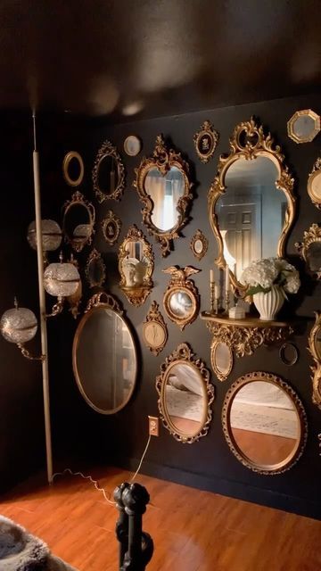 a taupe wall with a gallery wall of mirrors that feature gorgeous gold frames and a shelf with candles and blooms