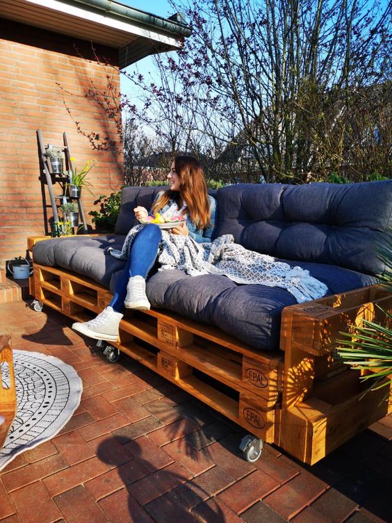 a terrace with a pallet sofa on casters, a boho rug, potted greenery is a cool and lovely space