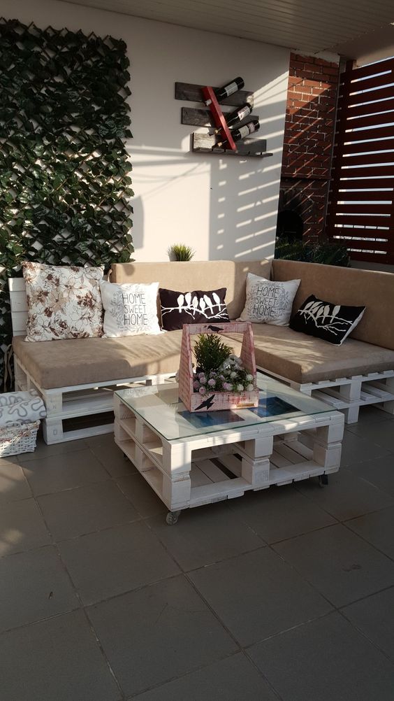 a terrace with a white pallet sofa and table, a living wall, some pillows and some cool decor