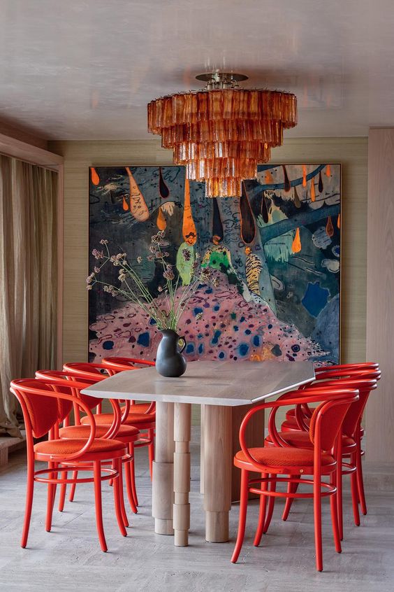 a vibrant dining room with a whimsical table, red chairs, a bold artwork dominating the space and an amber glass chandelier