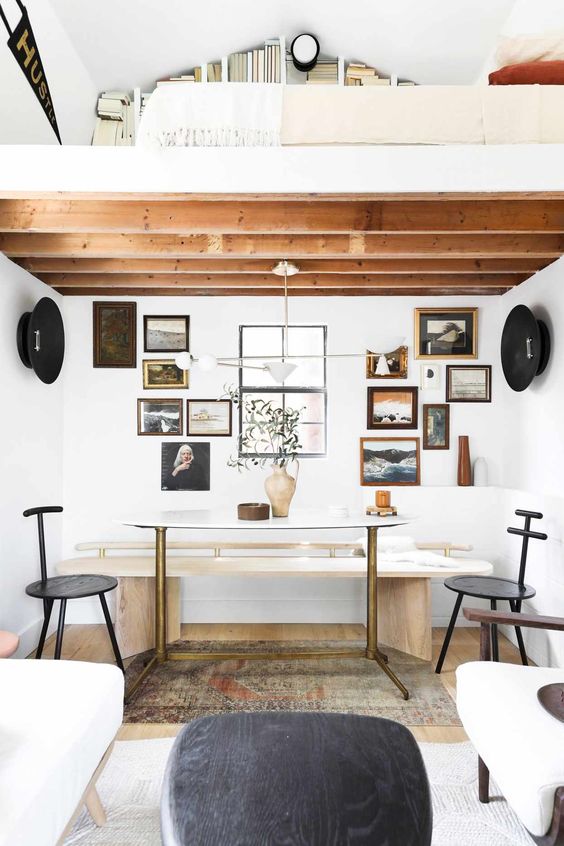 a welcoming shed home office with a loft space with books, a table that is a desk, black chairs, a gallery wall and white seating furniture