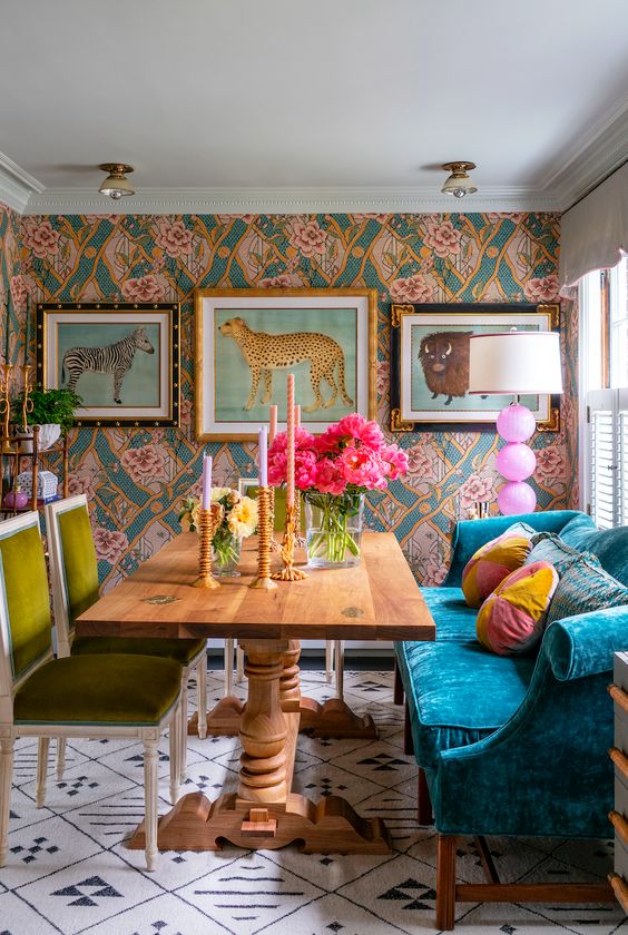 a whimsical and maximalist dining room with a printed wall, a navy sofa, mustard chairs, a vintage table and funny gallery wall plus a quirky floor lamp