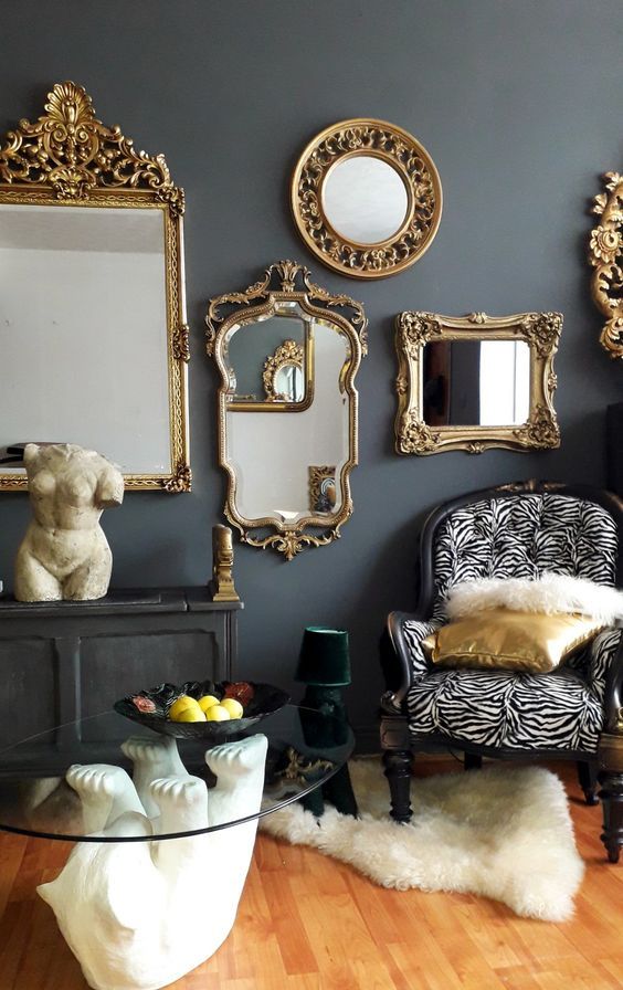 a whimsical and moody room with grey walls, mirrors in gorgeous gold frames, a printed chair, a black console table and a quirky coffee one