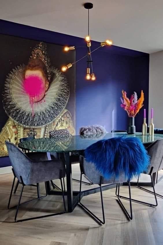 a whimsical dining room with a navy wall, a bold artwork, a glass table, grey chairs, colorful decor and faux fur