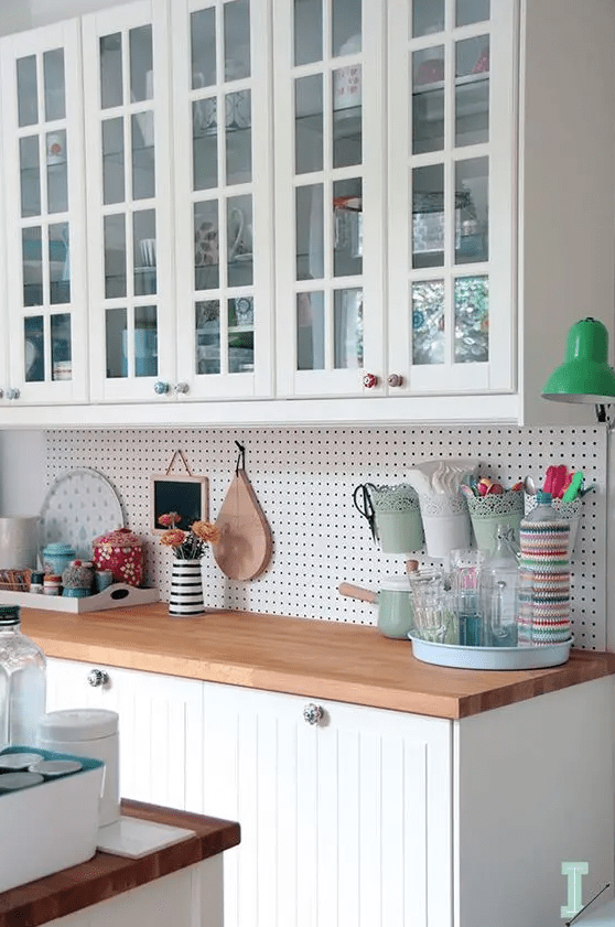 a white Scandinavian kitchen with planked and glass cabinets, a pegboard headboard and stained countertops plus some bright details