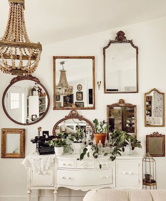 a white farmhouse space with a chic white console, a mirror gallery wall featuring gorgeous gold frames, a wooden bead chandelier and a neutral sofa