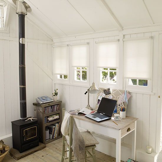 a white shed home office with a hearth, a reclaimed wood bookshelf, a vintage desk and a shabby chic chair, some decor and blooms