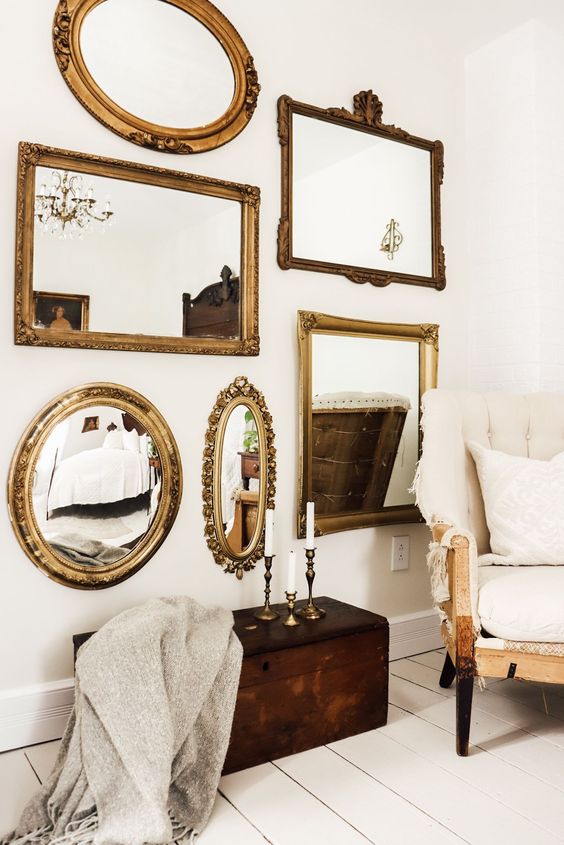 a white space with a creamy chair, a dark chest with decor and a refined mirror gallery wall with mirrors in gold frames