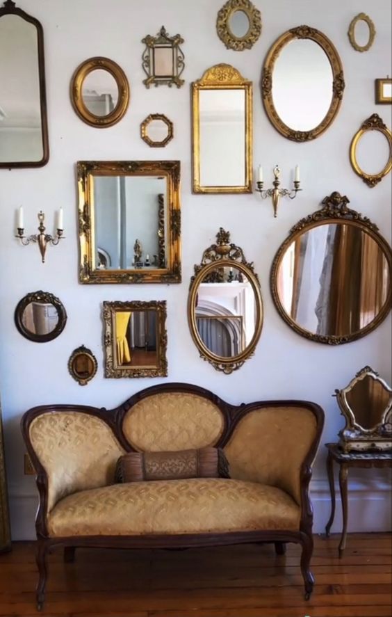 a white space with a refined loveseat and a chair, a mirror gallery wall with gold frames is a very sophisticated space