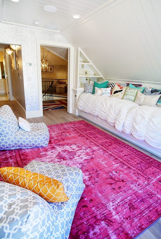 an attic bedroom with a bright pink rug, beanbag chairs, a bed with lots of pillows is a cool space