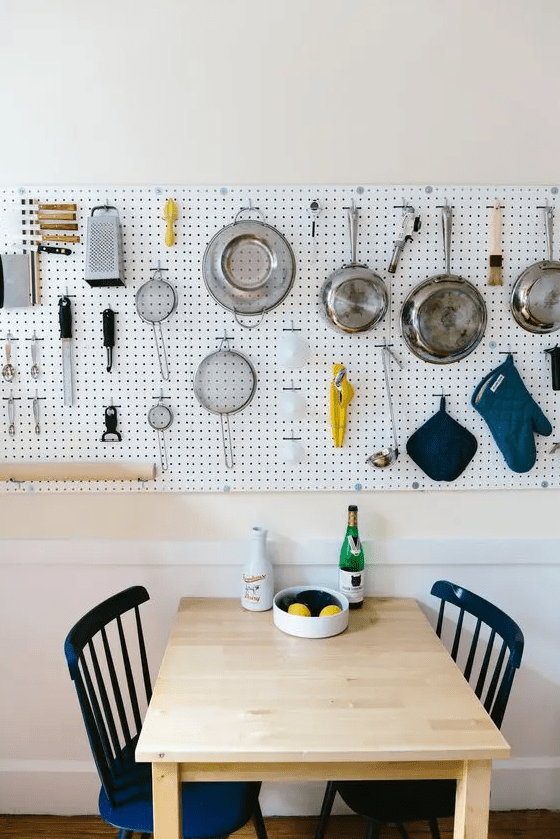 an eat-in kitchen with a long pegboard holding all kinds of kitchen ware and cookware is a cool space,a dn an eating space right here