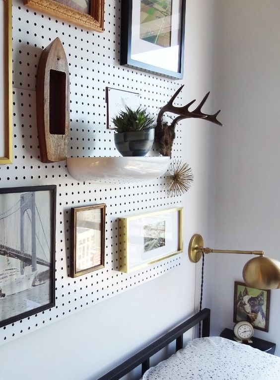 an oversized pegboard with shelves and art is used as a creative alternative to a headboard, it looks cool and impressive