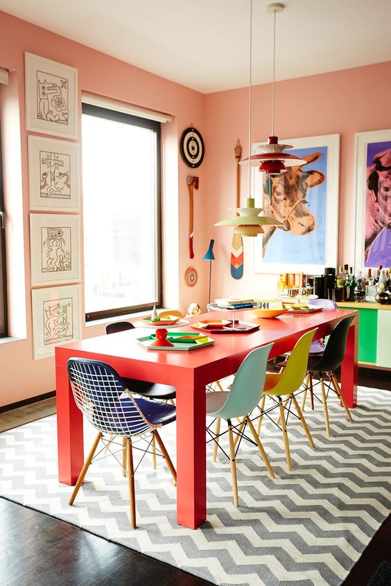 peachy walls, a red table, colorful chairs, bright artwork, a color block home bar compose a bold dining room