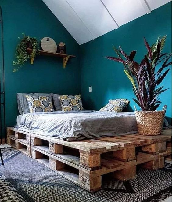 teal walls, a pallet bed with boho bedding, potted plants and some printed layered rugs compose a bold and cool bedroom