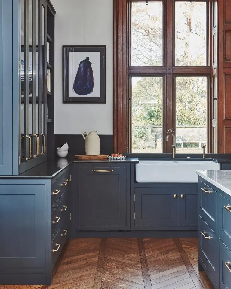 This beautiful kitchen is composed of navy cabinets, black countertops, gold handles and rich-stained frames and a cabinet add coziness to the space.