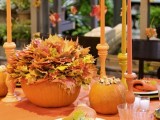 a brigth fall table setting with an orange tablecloth, bright candles, bold fall leaves and pumpkins
