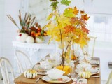 a neutral fall table with bright fall leaves in vases, natural pumpkins and neutral and stripes linens looks cool