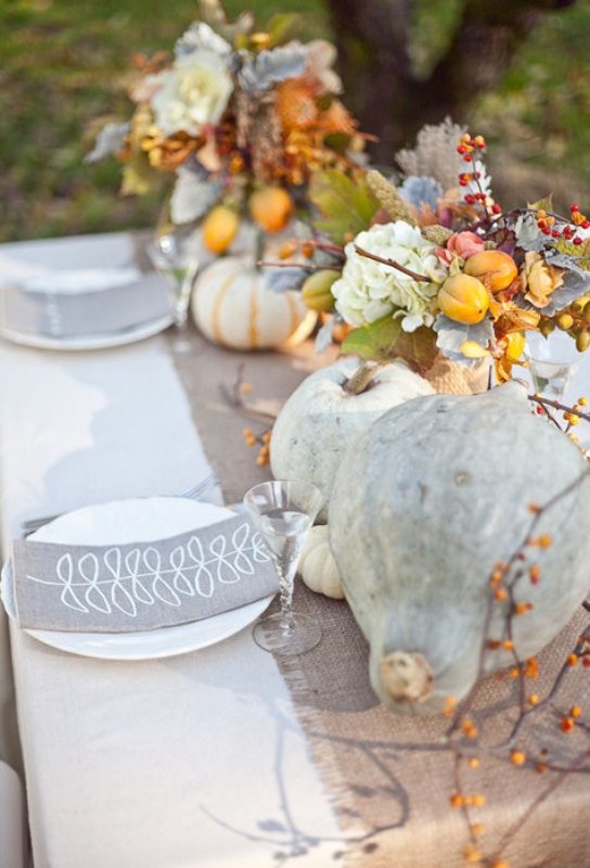 A beautiful fall table setting with neutral linens, real pale pumpkins, blooms, berries, fruits and printed napkins