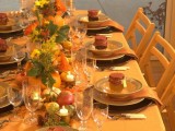 a bright fall table setting with bold and plaid linens, colorful candles and bold fall blooms and greenery in pumpkins