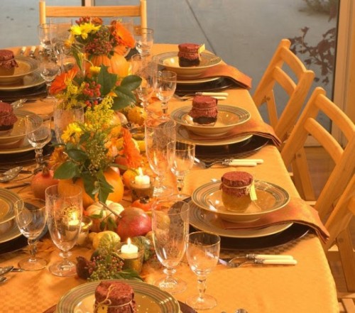 a bright fall table setting with bold and plaid linens, colorful candles and bold fall blooms and greenery in pumpkins