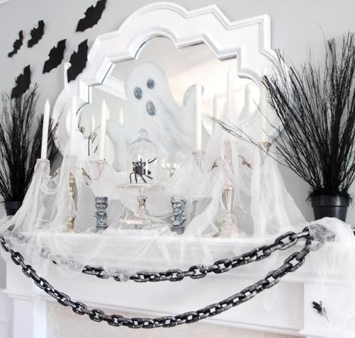 a Halloween mantel fully covered with tulle spiderweb, chunky chains, refined candleholders, black branches and black bats