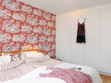 a white bedroom with a bright red printed wall as a bright highlight of the room