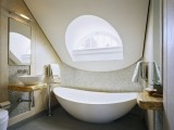 a neutral attic bathroom done with a large attic detail with a round window, an oval tub, floating shelves and vanities