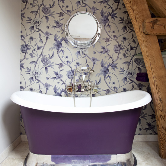a tiny yet colorful attic bathroom with a floral wallpaper wall, wooden beams, a purple tub looks cute and pretty
