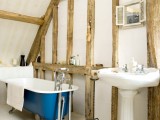 a cozy attic bathroom design with wooden beams, a blue vintage tub, a small window and a free-standing bathtub
