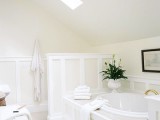 a neutral attic bathroom done in tan and white, with skylights, a shower space, a built-in tub and some blooms