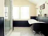 an elegant monochromatic bathroom with black paneling, a free-standing tub, a window, a shower enclosed in glass