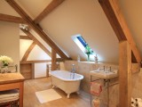 a warm and cozy attic rustic bathroom with wooden beams, neutral tiles, a free-standing tub and sink plus a cool wooden vanity
