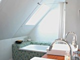 a small attic bathroom with white walls, a built-in tub clad with green tiles, a stained vanity with two sinks