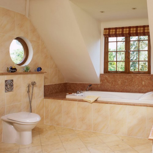 a warm attic bathroom clad with tiles in tan and brown, with several windows looks very inviting and cool