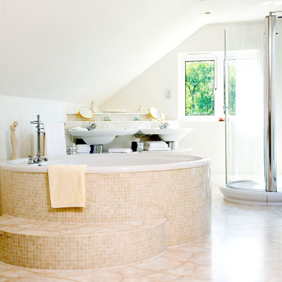 a neutral attic bathroom with tan tiles, a round tile clad bathtub, a shower space and a window for natural light