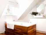 a modern attic bathroom with white walls, a window, a wooden floor and a wood clad bathtub