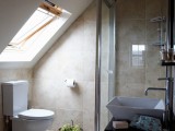 a small contemporary bathroom with a window, a shower space, a sink on a vanity and neutral tan tiles all over